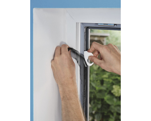 Person befestigt ein Insektenschutzgitter an einem Fensterrahmen mit einem Montagewerkzeug.