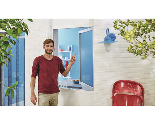 Ein Mann steht vor einem Fenster mit Insektenschutzgitter und zeigt darauf.