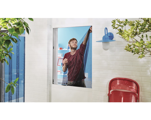 Mann montiert ein Insektenschutzgitter vor einem Fenster.