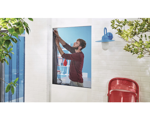 Mann befestigt ein Insektenschutzgitter an einem Fenster.