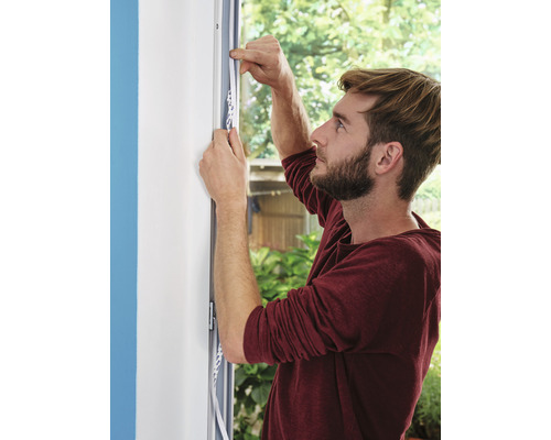 Mann befestigt Dichtungsband am Fensterrahmen zur Abdichtung.