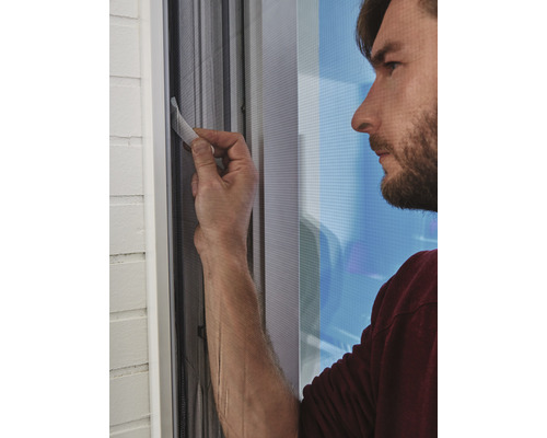 Mann befestigt ein Fliegengitter an einem Fensterrahmen