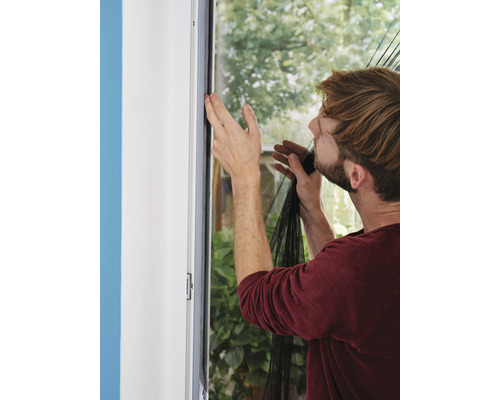Ein Mann befestigt ein Fliegengitter an einem Fensterrahmen.