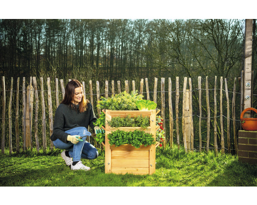 Frau arbeitet an einem dreistufigen Kräuterbeet aus Holz im Garten