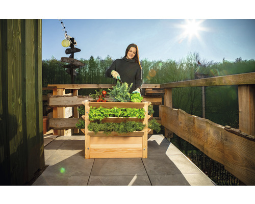 Frau gärtnert im Hochbeet auf einem Balkon mit Holzzaun.