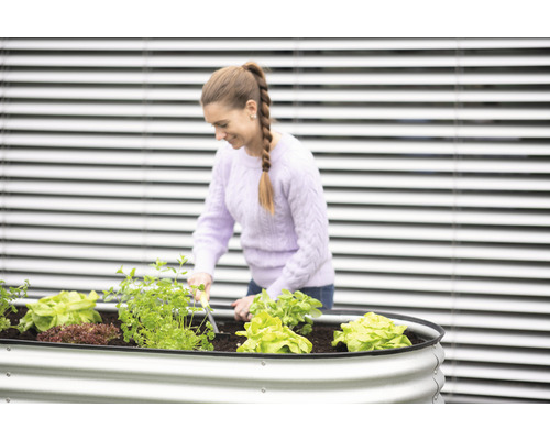Frau arbeitet im Hochbeet mit Salat und Kräutern