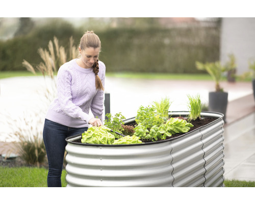 Frau arbeitet im Garten mit einem Hochbeet aus Metall und verschiedenen Gemüsesorten.
