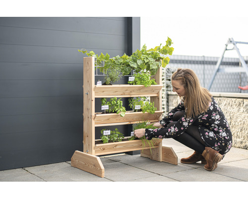 Eine Frau erntet Kräuter von einem Holz-Kräuterregal auf einer Terrasse