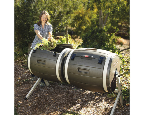 Frau befüllt einen doppelten Komposttumbler im Garten mit Gartenabfällen.