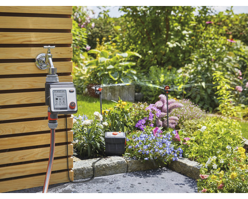Gartenszene mit Wasserhahn, Bewässerungssteuerung und Rasensprenger