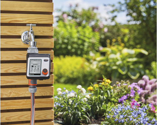 Bewässerungssteuerung mit Wasserhahnanschluss und Gartenschlauch vor Gartenkulisse