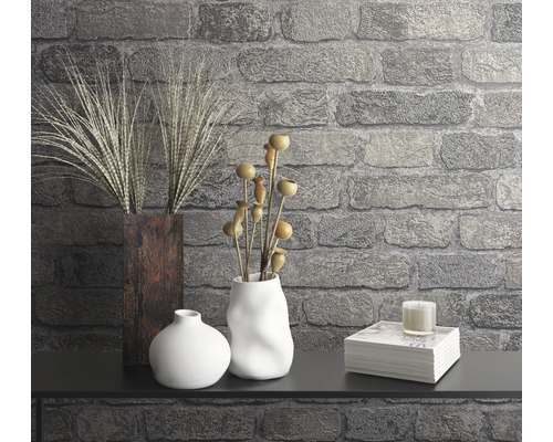 Dekorative Szene mit Vasen, Pflanzen, Kerze und Bücherstapel vor einer Steinwand.