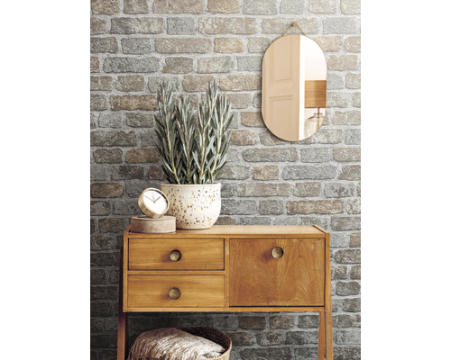 Dekoratives Interieur mit gemusterter Backstein Tapete, Holzkommode, Spiegel und Zimmerpflanze.