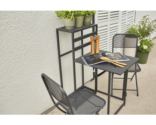 Gartenszene mit Tisch, zwei Stühlen und einem Pflanzenständer auf einer Terrasse.