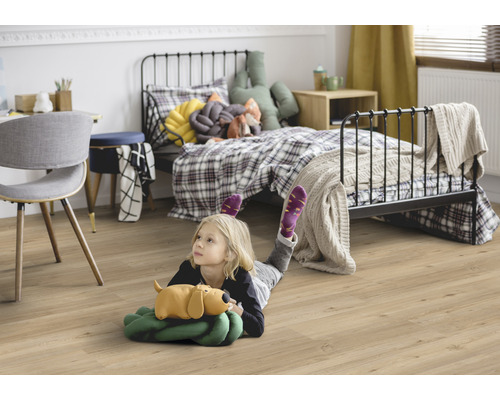 Kind liegt auf einem Laminatboden in einem Kinderzimmer mit Bett und Schreibtisch