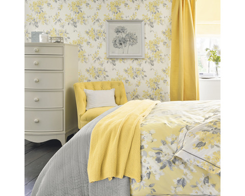 Helles Schlafzimmer mit floraler Tapete, Kommode, Sessel und Bettwäsche