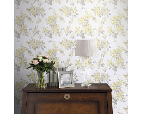 Szene mit floral gemusterter Tapete, Tisch, Lampe, Blumen und Bilderrahmen