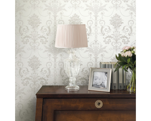 Dekoratives Interieur mit gemusterter Tapete, Lampe, Bilderrahmen, Büchern und Blumen auf einem Schrank.