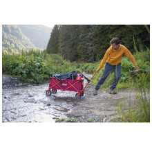 Mann zieht einen roten Bollerwagen mit Gepäck über einen Weg in der Natur