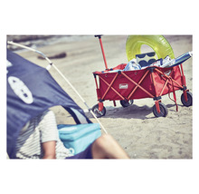 Strandszene mit Strandmuschel und rotem Bollerwagen von Coleman, beladen mit Strandutensilien