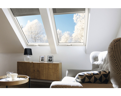 Helles Dachzimmer mit Dachfenstern und Rollos, eingerichtet mit Kommode, Lampe und Sessel