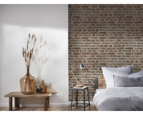 Schlafzimmer mit Bett vor einer Backsteinmauer und Dekoration auf einem Holztisch