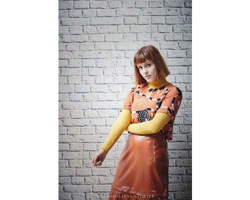 Frau mit gemustertem T-Shirt und glänzendem Rock vor einer Ziegelwand