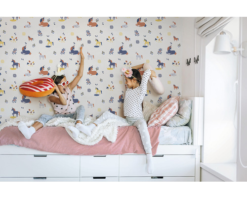 Zwei Mädchen sitzen auf einem Bett vor einer Wand mit Einhornmuster.