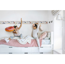 Zwei Mädchen sitzen auf einem Bett mit weißem Rahmen und Schubladen vor einer Wandbordüre mit Einhornmotiv