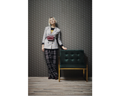 Frau in Jacke und Hose neben Sessel und geometrischer Tapete
