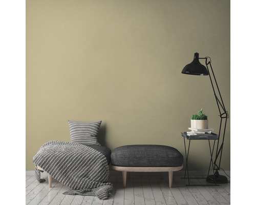 Dekoratives Wohnambiente mit Sitzgelegenheit, Stehlampe und Zimmerpflanze auf Beistelltisch vor einfarbiger Wand