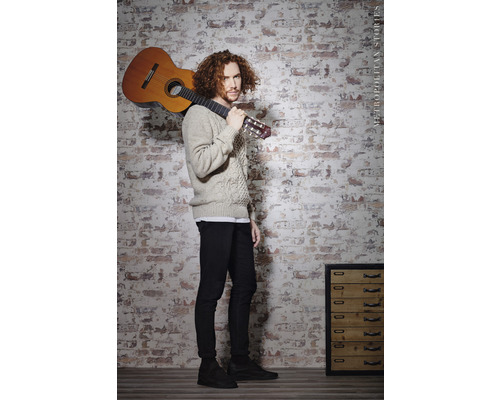 Mann mit Gitarre vor einer Ziegelwand