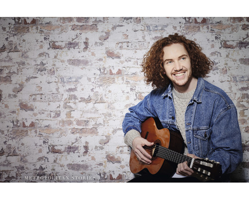 Mann mit Gitarre vor einer Ziegelwand
