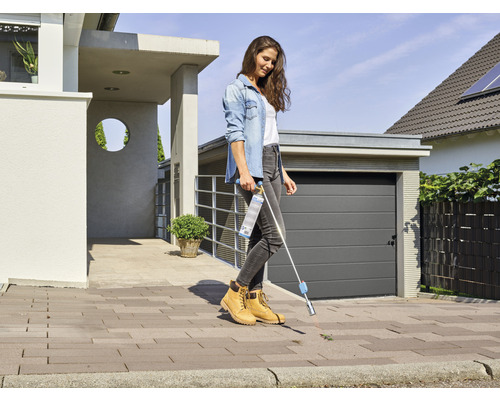 Eine Frau entfernt Unkraut mit einem Unkrautentferner vor einem Haus.