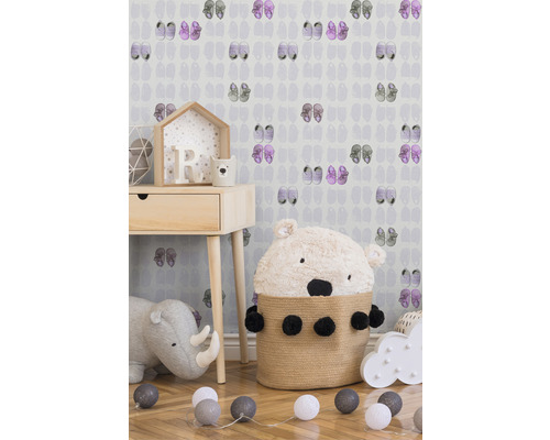 Kinderzimmer mit Nachttisch, Stofftier und dekorativer Beleuchtung vor einer Tapete mit Schuhmotiv.