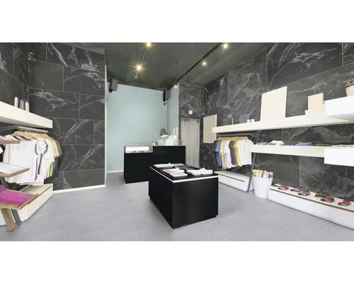 Innenraum eines Bekleidungsgeschäfts mit Fliesenwänden in Marmoroptik, Kleiderständern und Verkaufsfläche.