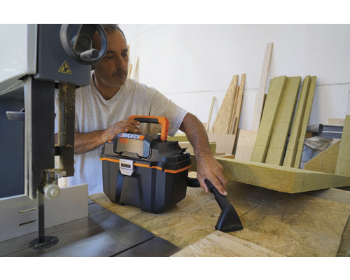 Handwerker benutzt Nass Trockensauger am Werkstatttisch mit Bandsäge und Holzresten