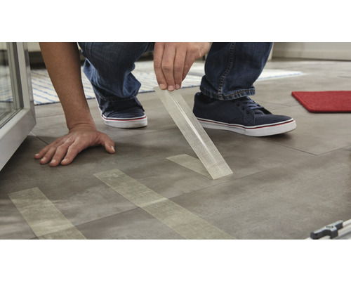 Mann verlegt Fliesen mit Klebeband zur Befestigung