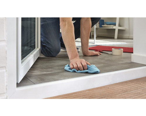 Eine Person wischt den Boden mit einem Tuch in Bodennähe eines Fensters.