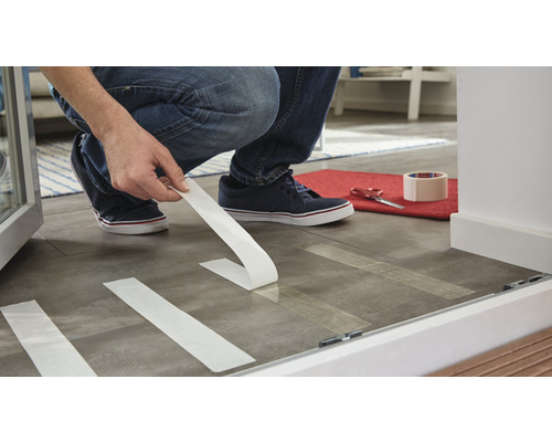 Person klebt Klebeband auf Boden