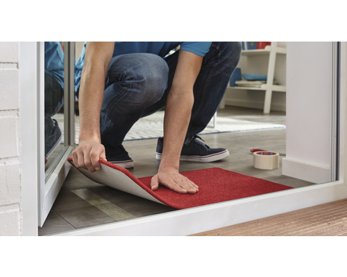 Person verlegt eine rote Fußmatte im Innenbereich