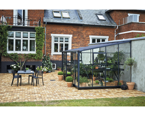 Gartenansicht mit Gewächshaus, Tisch und Stühlen auf gepflasterter Terrasse