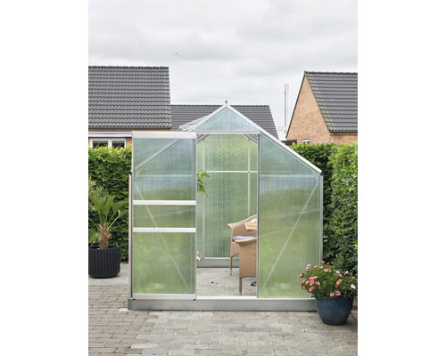 Gewächshaus mit geöffneter Tür auf einer Terrasse mit Gartenmöbeln und Pflanzen