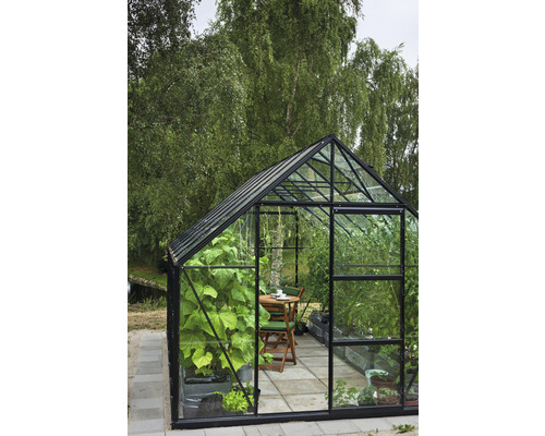 Gewächshaus mit Pflanzen und Sitzgruppe im Garten.