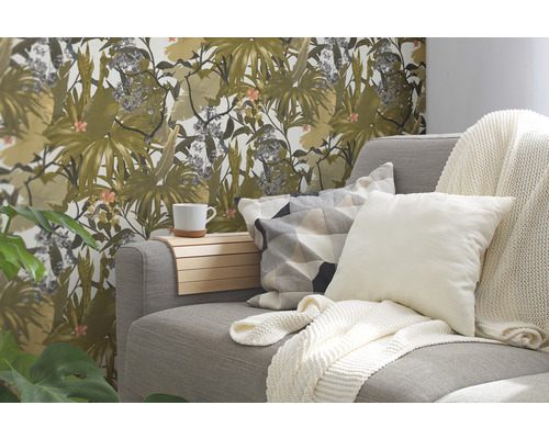 Wohnzimmer mit grauer Couch, Kissen, Decken und einer Wand mit floraler Tapete.