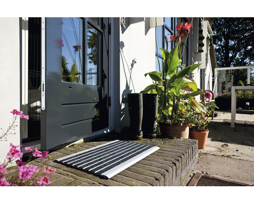 Fußmatte vor einer Haustür mit Pflanzen und Gummistiefeln