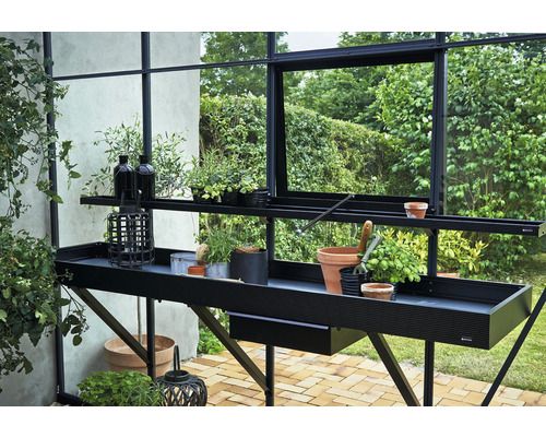 Gartentisch mit Pflanzen und Gartenzubehör in einem Gewächshaus