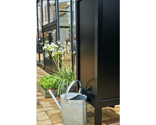 Regenwassertank mit Gießkanne und Pflanzen vor einem Gewächshaus