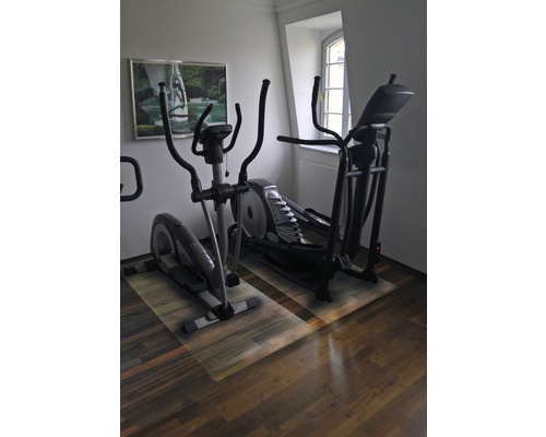 Zwei Crosstrainer in einem Raum mit Holzboden und einem Fenster.