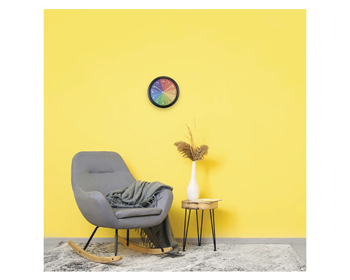 Wohnraum mit Schaukelstuhl, Wanduhr und Beistelltisch vor gelber Wand